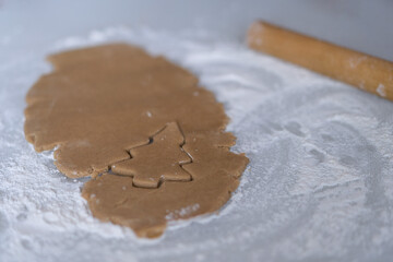 The cookie shape is cut out on the dough in the form of a Christmas tree.