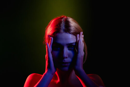 Female silhouette portrait. Feeling exhausted. Frustrated woman in neon light glow holding head looking at camera isolated on black. Headache pain. Stuck problem. Toxic relationship