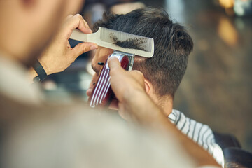 Careful barber working with electric hair clipper at a barbershop