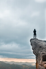 silhouette of the strong man at the edge of the cliff in mountains