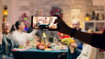 Girl taking a family portrait with her phones while celebrating christmas. Traditional festive christmas dinner in multigenerational family. Enjoying xmas meal feast in decorated room. Big family - Powered by Adobe