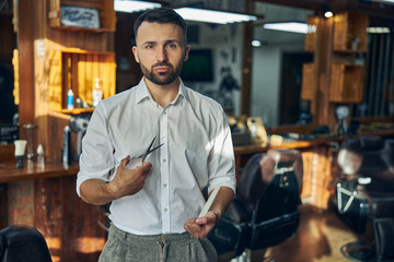 Fototapeta premium Young hair-stylist looking professional at his workplace