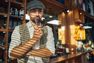 Professional male hair-stylist looking pensive with his straight razor