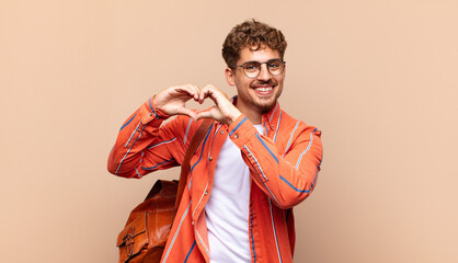 young man smiling and feeling happy, cute, romantic and in love, making heart shape with both...