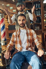 Obraz na płótnie Canvas Stylish barber and hipster client posing at a barbershop