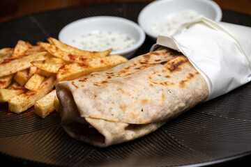 Shawerma on the black plate, Doner-kebab Lavash with barbecue Durum Gyros Brtuch Burrito Enchilada Taco Tantuni Quesadilla Fajitas white sauce, french fries, meet, fish, seafood on the black plate
