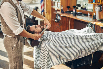 Young customer at a barbershop getting his beard groomed