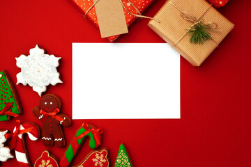 Blank sheet of paper with Christmas gift and gingerbread cookies on red background