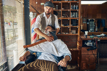 Fashionable hairdresser shaving his customer with an axe