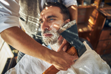Handsome young man being shaved with an axe