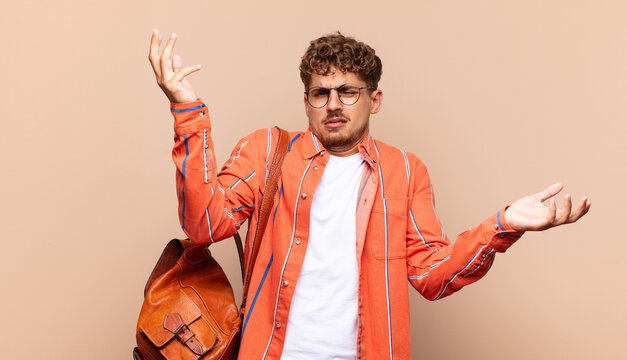 young man shrugging with a dumb, crazy, confused, puzzled expression, feeling annoyed and clueless. student concept