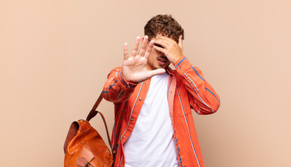 young man covering face with hand and putting other hand up front to stop camera, refusing photos...
