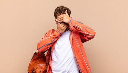 young man covering face with both hands saying no to the camera! refusing pictures or forbidding...