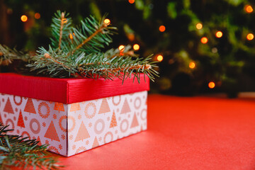 Christmas gift box with spruce branch on the red table . Christmas tree with bokeh on the background