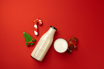 Glass milk bottle and Christmas gingerbread cookies on red background