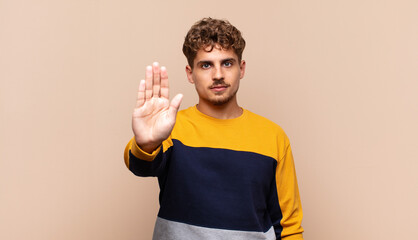 young man looking serious, stern, displeased and angry showing open palm making stop gesture