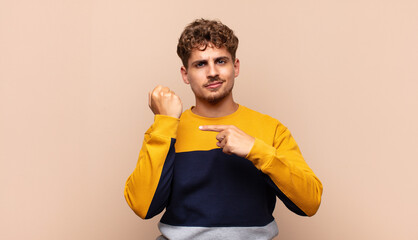 young man looking impatient and angry, pointing at watch, asking for punctuality, wants to be on...
