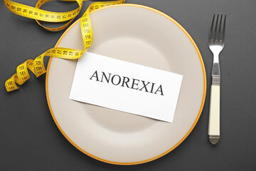 Plate with word ANOREXIA and measuring tape on dark background