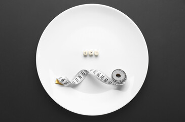 Plate with word EAT and measuring tape on dark background. Concept of anorexia