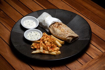 Shawerma on the black plate, Doner-kebab Lavash with barbecue Durum Gyros Brtuch Burrito Enchilada Taco Tantuni Quesadilla Fajitas white sauce, french fries, meet, fish, seafood on the black plate