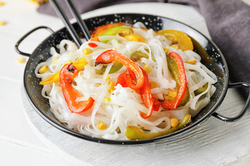 Frying pan with tasty rice noodles and vegetables on table