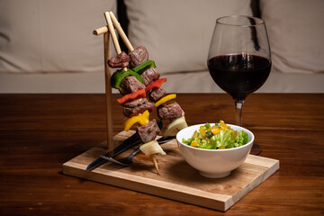 Meat beef shish kebab with vegetables and spices on a dark background on a wooden cutting board. Shish kebab BBQ meat. Fish kebab with bell pepper. French fry. Salad. Glass red wine. Dark wood table.