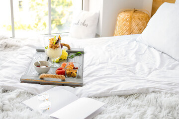 Tray with tasty breakfast and book on bed