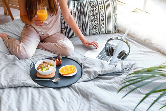 Young woman with laptop having tasty breakfast in bed