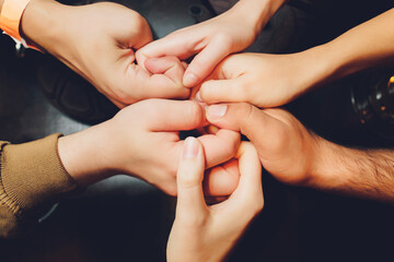 two man and three women holding hands on a table implying a polyamory relationship or love triangle.