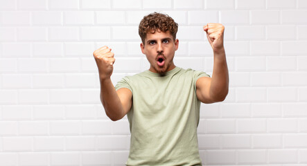 young man celebrating an unbelievable success like a winner, looking excited and happy saying take...