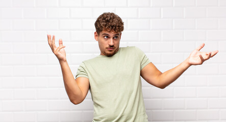 young man shrugging with a dumb, crazy, confused, puzzled expression, feeling annoyed and clueless