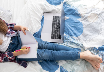 Distance learning online education. Schoolgirl studying at home with digital laptop notebook and doing school homework lying on bed at home.