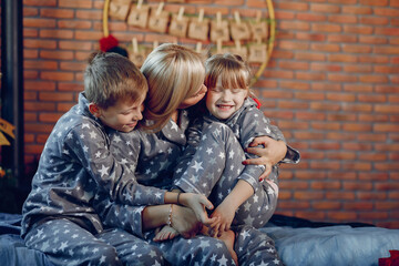 Beautiful mother in a gray pajamas. Family sitting on a bed. Little girl and boy near christmas tree