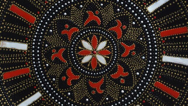 Decorative ceramic plate with red and golden colors, painted plate is rotating on background, close up, top view. Decorative porcelain plate painted with acrylic paints, handwork, dot painting