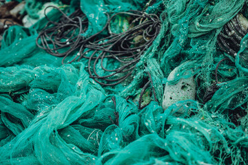 Close up view pile of green nylon multi colorful bright fish nets with pieces of white corals and old ropes in fishing village. Still life background pattern. Hobby fishing concept. Copy space