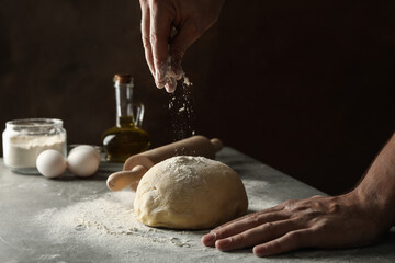 Man sprinkle flour on dough against dark background