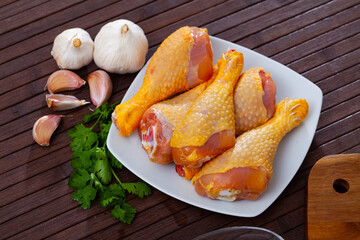Home cooking. Fresh raw chicken drumsticks and condiments prepared for roasting on wooden table