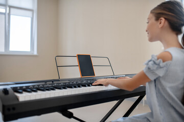 Long-haired girl in blue dress sitting at the synthesizer and exercising