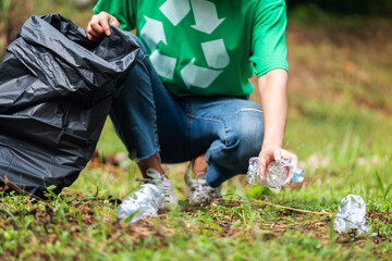 Closeup image of a female activist picking up garbage plastic bottles into a plastic bag in the park for recycling concept