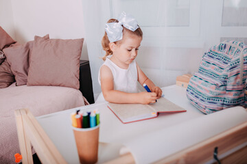 Little girl in the school near the school desk. A girl writes in notebook. School supplies on the desk.