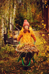 Happy child girl working in autumn garden, helps to remove fall leaves from lawn