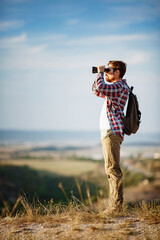 Guy looking at binoculars in hill. man in t-shirt with backpack.