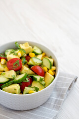 Fresh Avocado Tomato Salad in a bowl on a white wooden background, low angle view. Copy space.