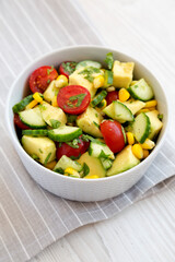 Fresh Avocado Tomato Salad in a bowl on a white wooden background, low angle view.