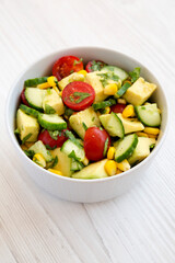 Fresh Avocado Tomato Salad in a bowl on a white wooden background, side view.