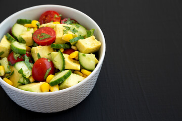 Fresh Avocado Tomato Salad in a bowl on a black surface, side view. Copy space.