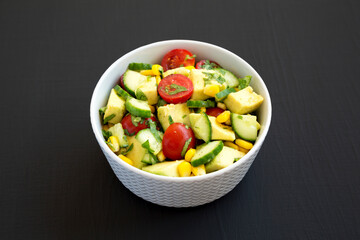 Fresh Avocado Tomato Salad in a bowl on a black background, side view.