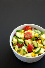 Fresh Avocado Tomato Salad in a bowl on a black background, side view. Copy space.