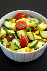 Fresh Avocado Tomato Salad in a bowl on a black background, side view. Close-up.