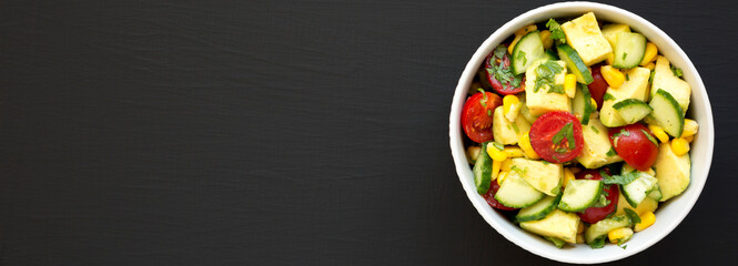 Fresh Avocado Tomato Salad in a bowl on a black surface, top view. Flat lay, overhead, from above. Copy space.